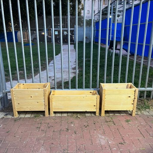 קומפוסטר עץ בגינה קהילתית לצד אדניות פורחות.